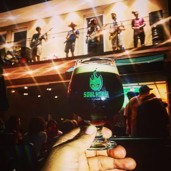 Taça de cerveja escura Soul Hops com a banda tocando na varanda ao fundo
