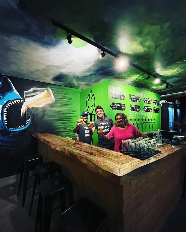 Equipe brindando no balcão do Soul Hops Camburizinho, com o mural do tubarão